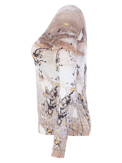 A sculptural, abstract wall sculpture on a solid white background. The piece features a textured, organic form with a color palette of beige, brown, white, black, and small gold splatters.