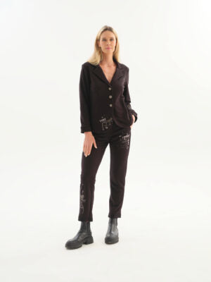 A woman modeling a dark brown two-piece pajama set with embroidered details, consisting of a long-sleeve button-up top and matching pants, paired with black boots, against a plain white studio background.
