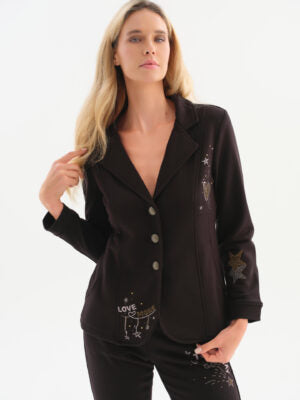 A woman modeling a black long-sleeve blazer with embroidered celestial and text details, paired with matching black pants, against a plain white studio background.