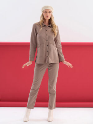 A woman modeling a matching taupe two-piece lounge set consisting of a long-sleeve button-up shirt and straight-leg pants, styled with a beige beret and off-white ankle boots against a studio backdrop with a red lower section.
